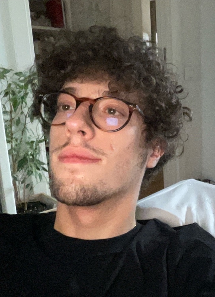 Edoardo, curly hair and round glasses, looking off to the side